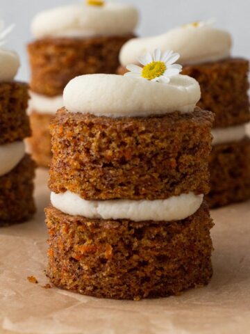 Small carrot cakes stacked with cream cheese frosting and topped with fresh chamomile flowers.