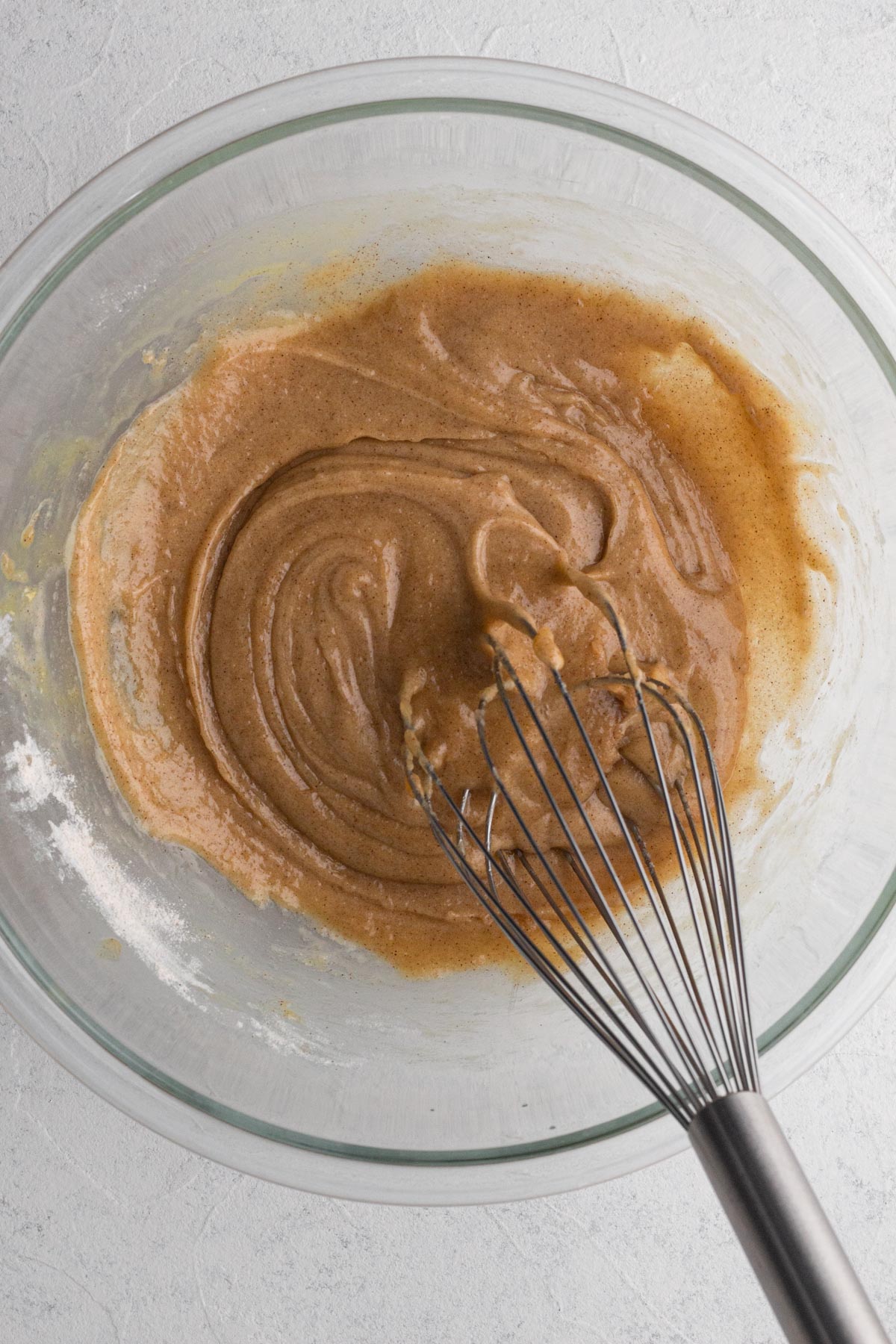 Cake batter in a glass mixing bowl with a metal whisk.