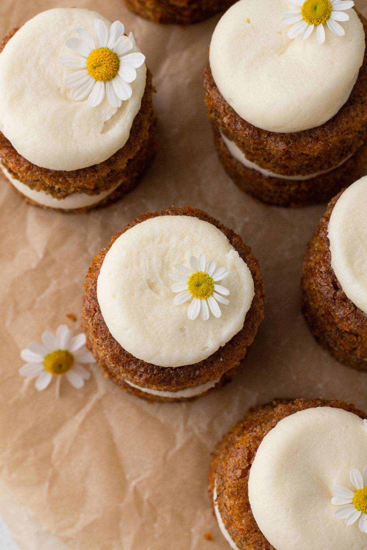 Overhead view of tiny carrot cakes topped with cream cheese frosting and fresh chamomile flowers.