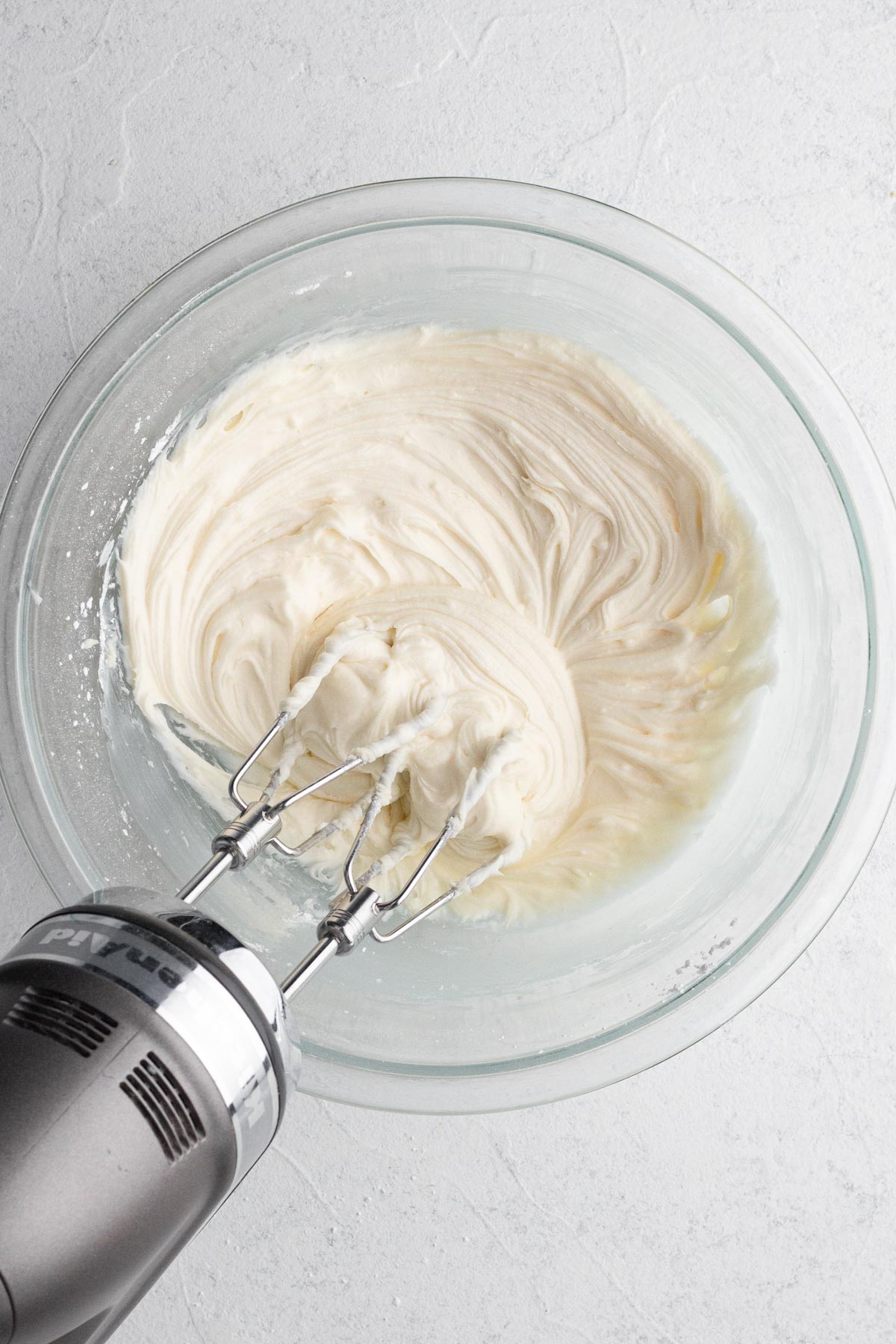 Frosting in a glass mixing bowl with an electric hand mixer.
