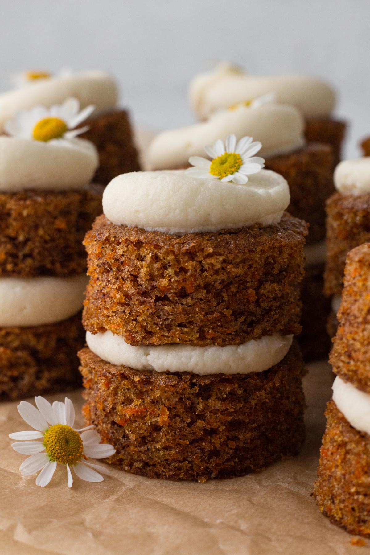Tiny carrot cakes stacked with cream cheese frosting and topped with fresh chamomile flowers.