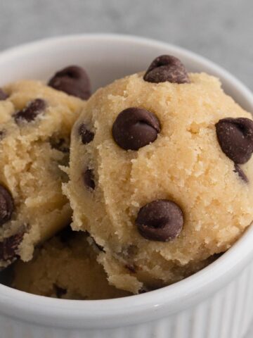 Close up view of scoops of chocolate chip cookie dough in a white ramekin on a gray surface.