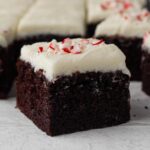 A square slice of chocolate cake topped with white frosting and crushed candy canes.