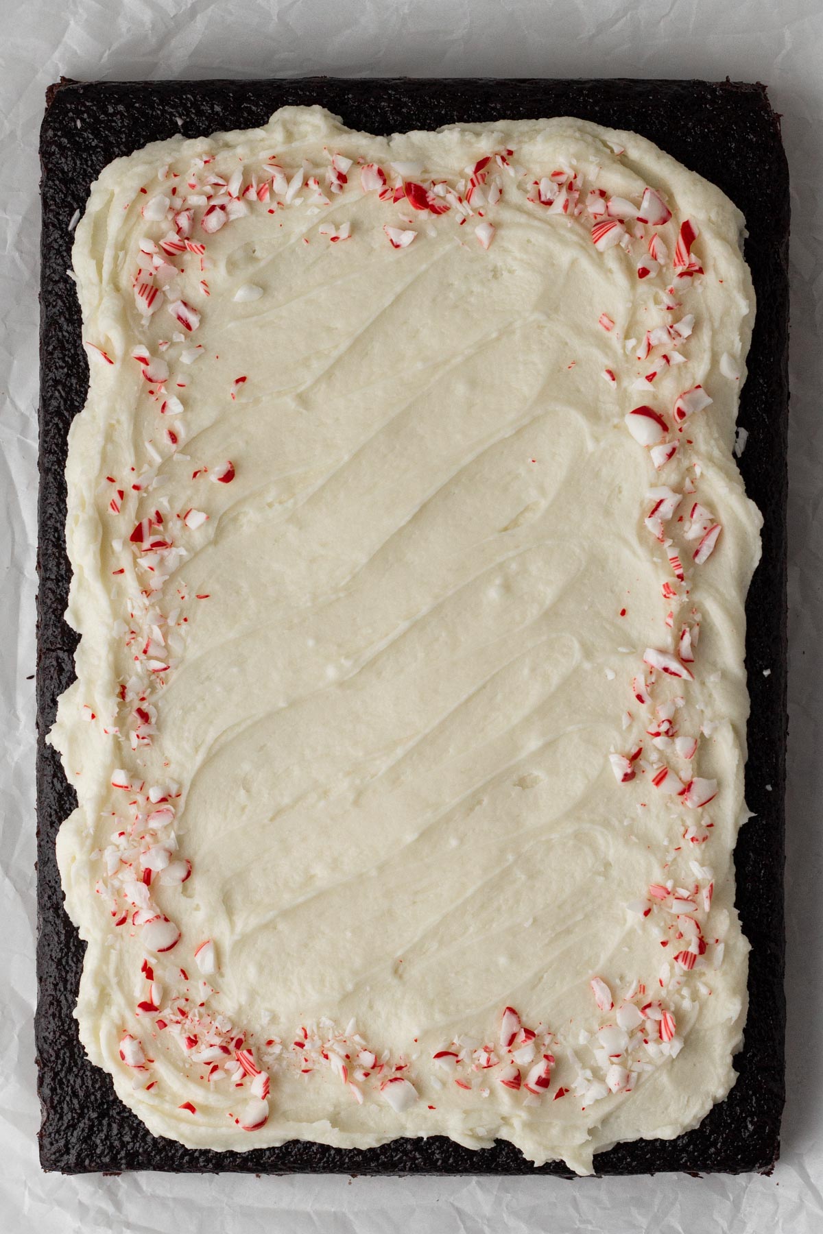 Chocolate sheet cake decorated with white frosting and crushed candy canes.