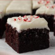 Side view of a square slice of chocolate cake topped with white frosting and crushed candy canes with a text overlay.