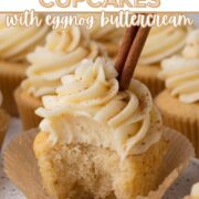 A bitten cupcake topped with a swirl of frosting garnished with a cinnamon stick with a text overlay.