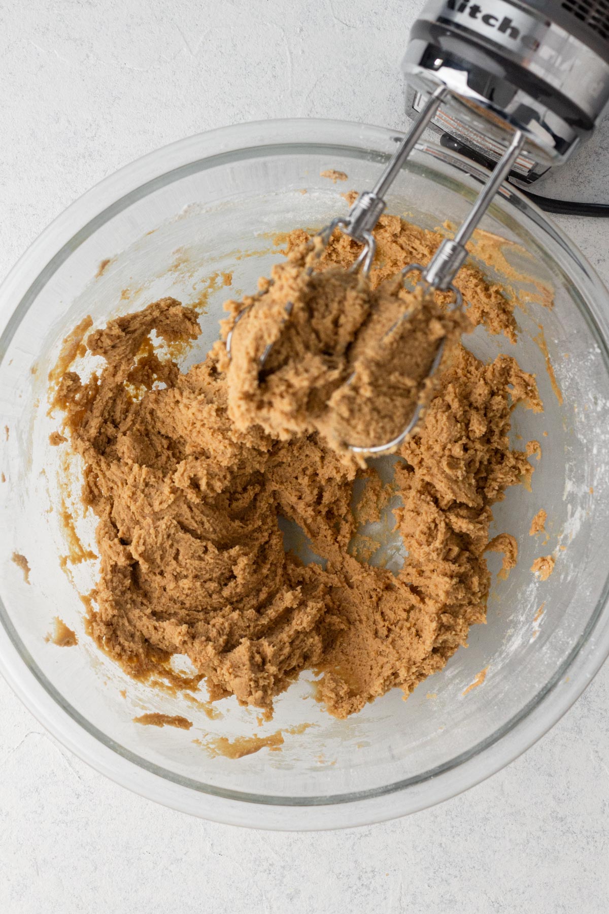 Cookie dough in a glass mixing bowl with an electric hand mixer.
