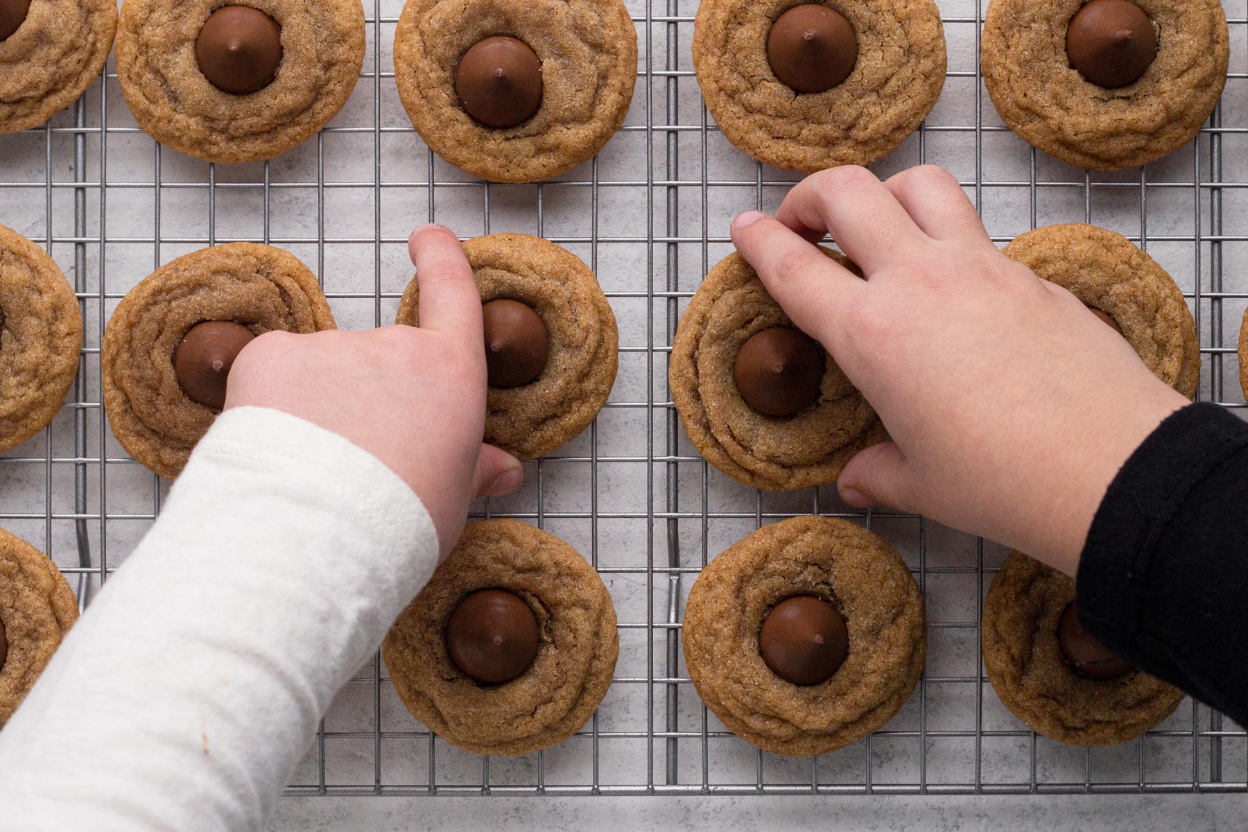 Hands of young children reaching for cookies on a wire cooling rack.