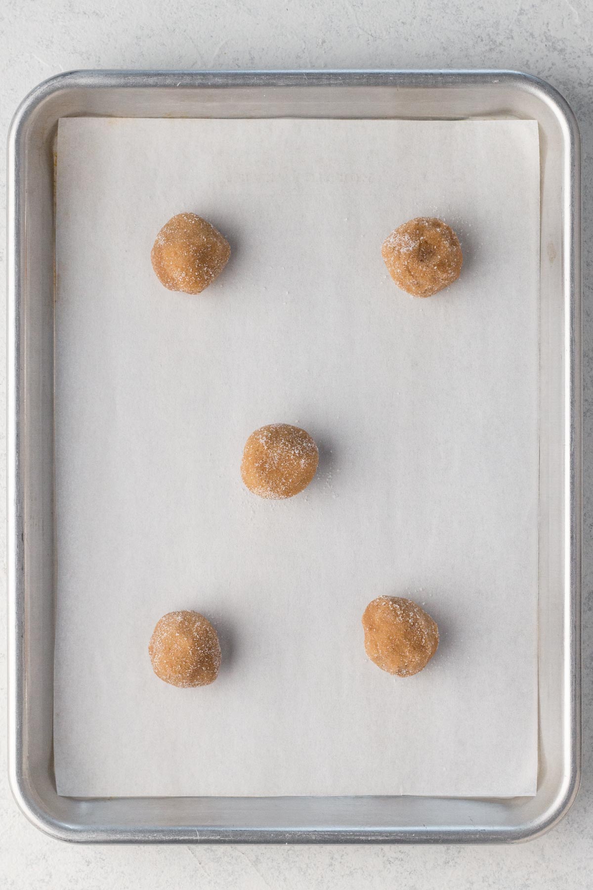 Balls of cookie dough rolled in sugar on a baking sheet lined with parchment paper.
