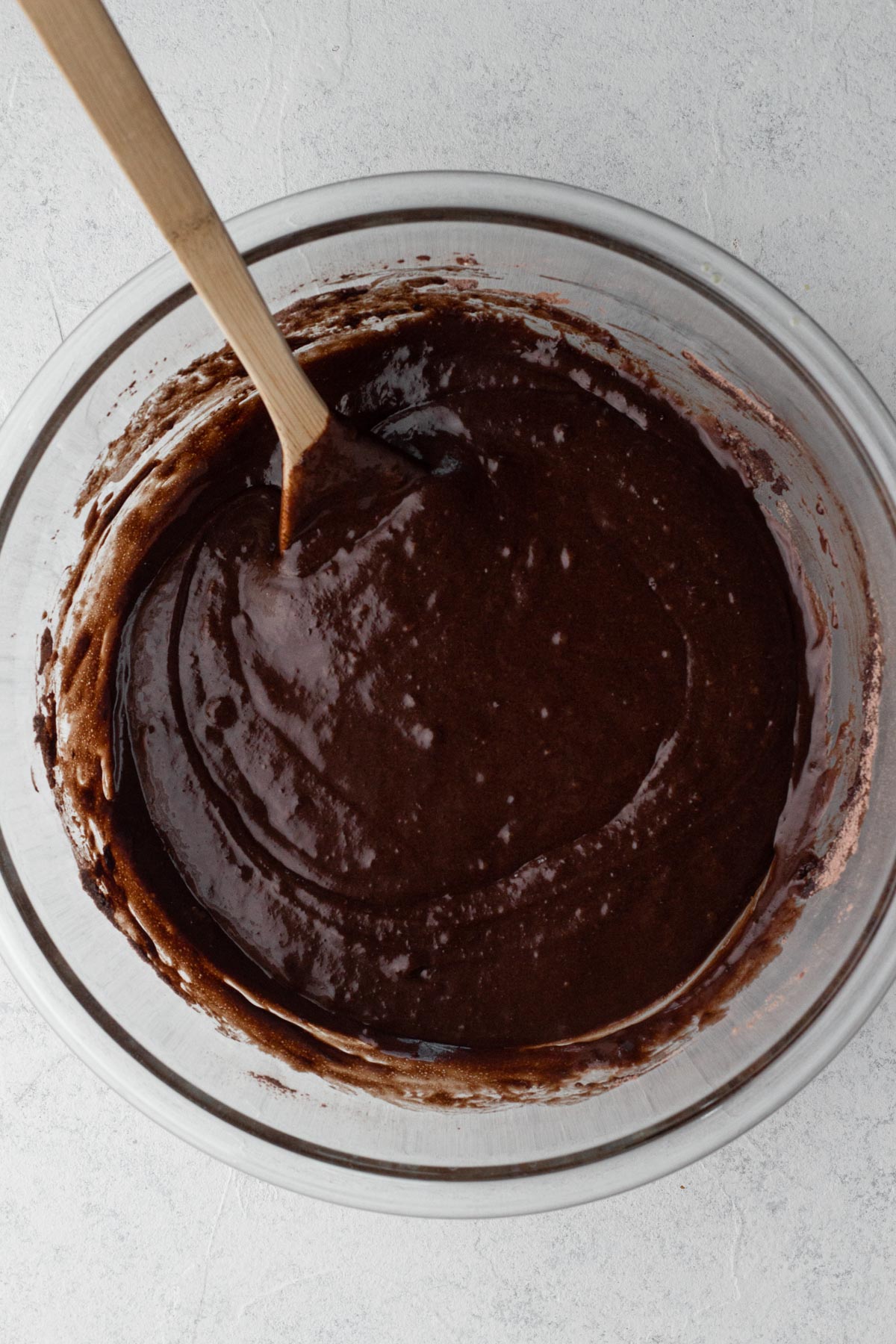 Wet and dry ingredients stirred together in a glass mixing bowl with a wooden spoon.