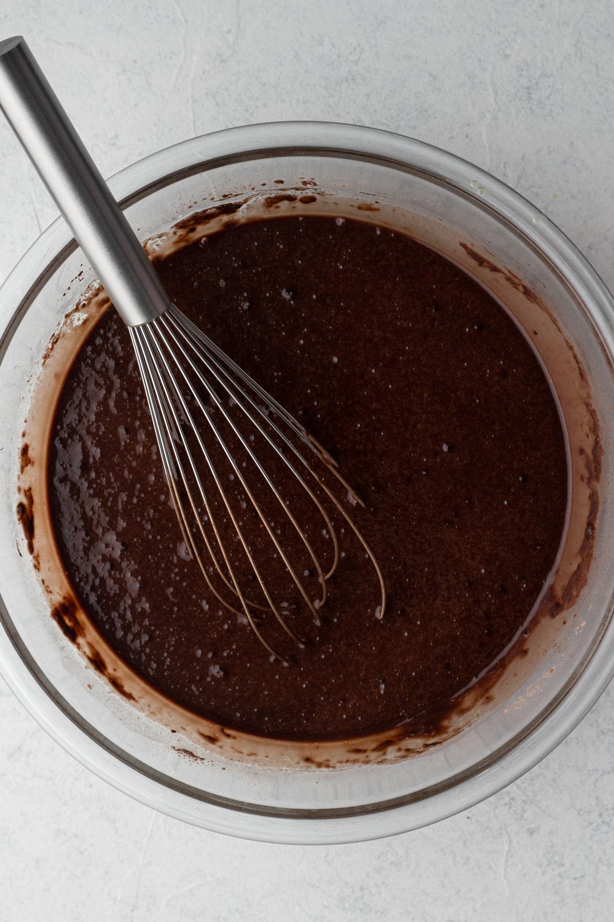 Cake batter in a glass mixing bowl with a metal whisk.