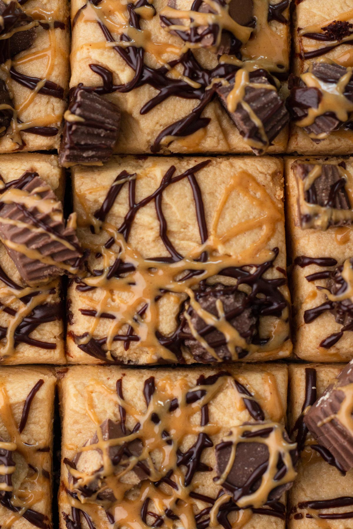 Close-up view of square cake slices topped with peanut butter frosting, peanut butter cups, and chocolate drizzle.