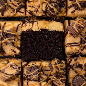 Close-up view of square slices of chocolate cake topped with peanut butter frosting, peanut butter cups, and drizzles of chocolate and peanut butter.
