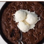Brownie with chocolate chips and scoops of vanilla ice cream in a cast iron skillet with a text overlay.