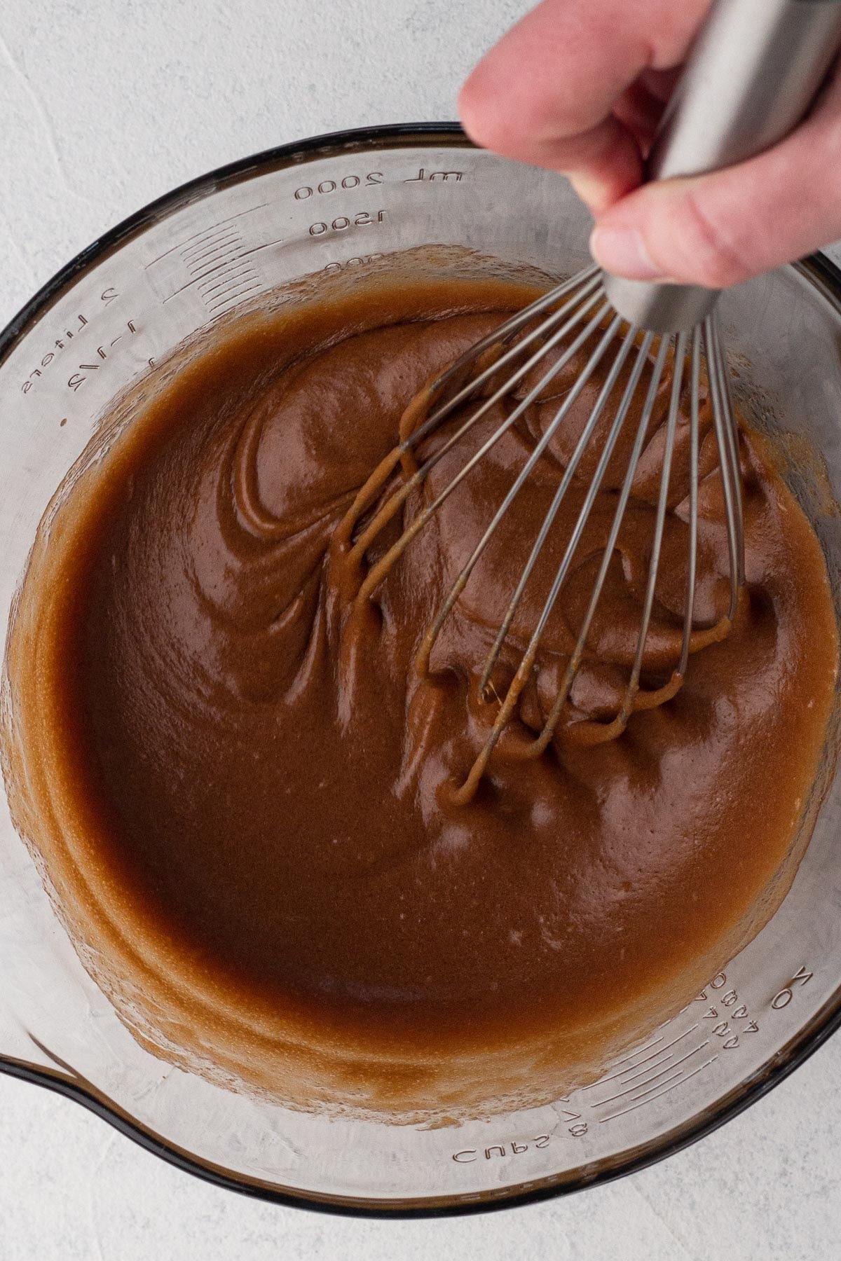 Hand whisking wet ingredients in a glass batter bowl.