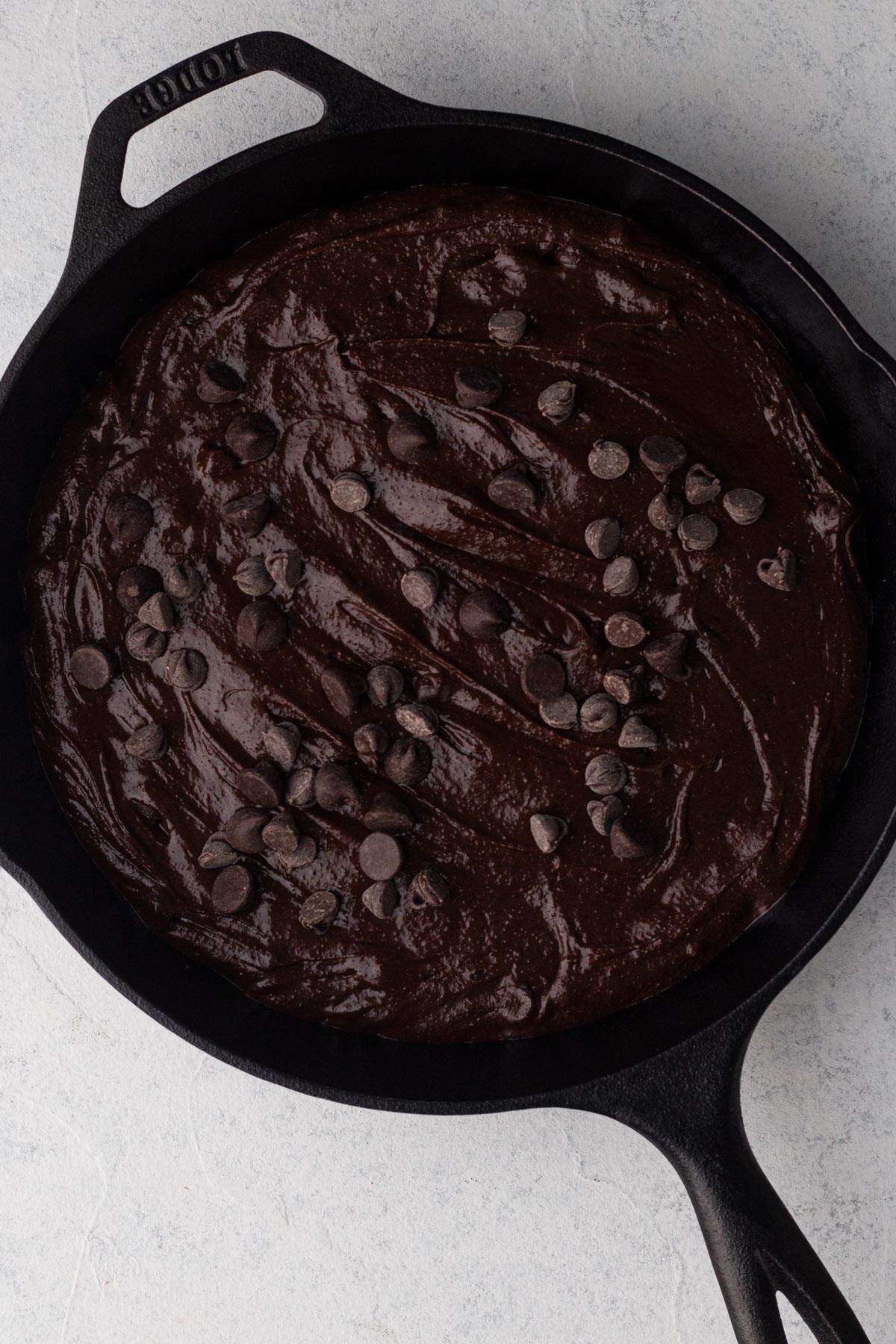 Brownie batter with chocolate chips in a cast iron skillet.