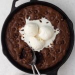 Brownie with chocolate chips and scoops of vanilla ice cream in a cast iron skillet.