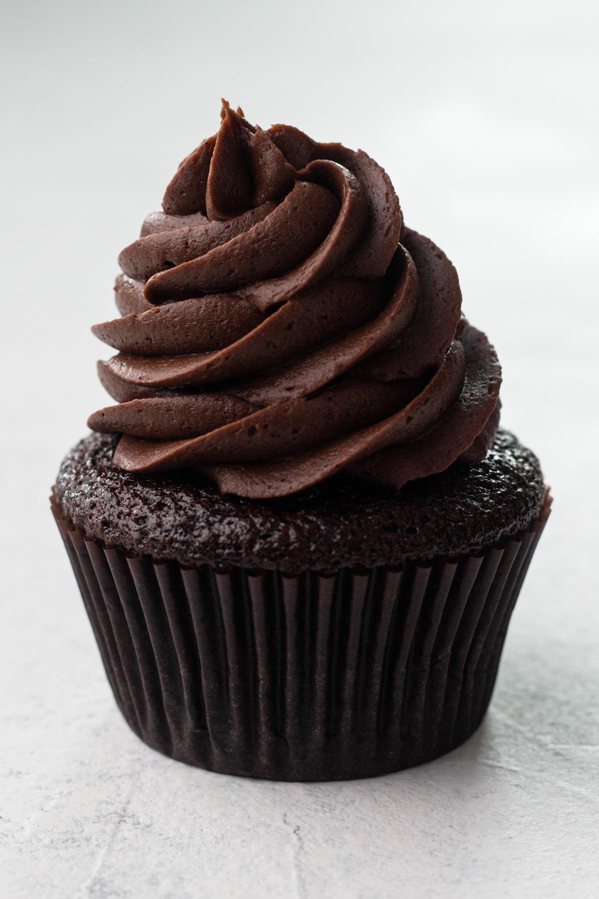 A chocolate cupcake topped with a swirl of chocolate frosting on a white background.