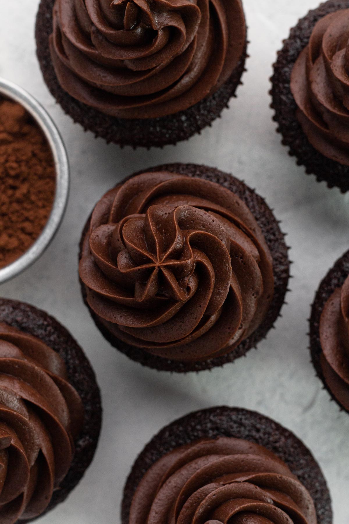 An overhead view of chocolate cupcakes topped with swirls of chocolate frosting.