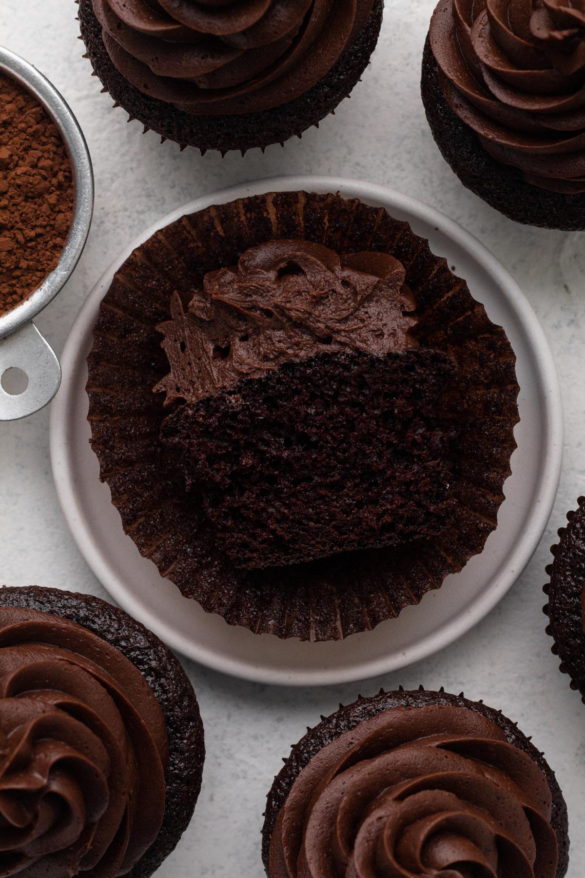 A chocolate cupcake with chocolate frosting cut in half on a white plate.