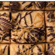 Close-up view of square cake slices topped with peanut butter frosting, peanut butter cups, and chocolate drizzle with a text overlay.