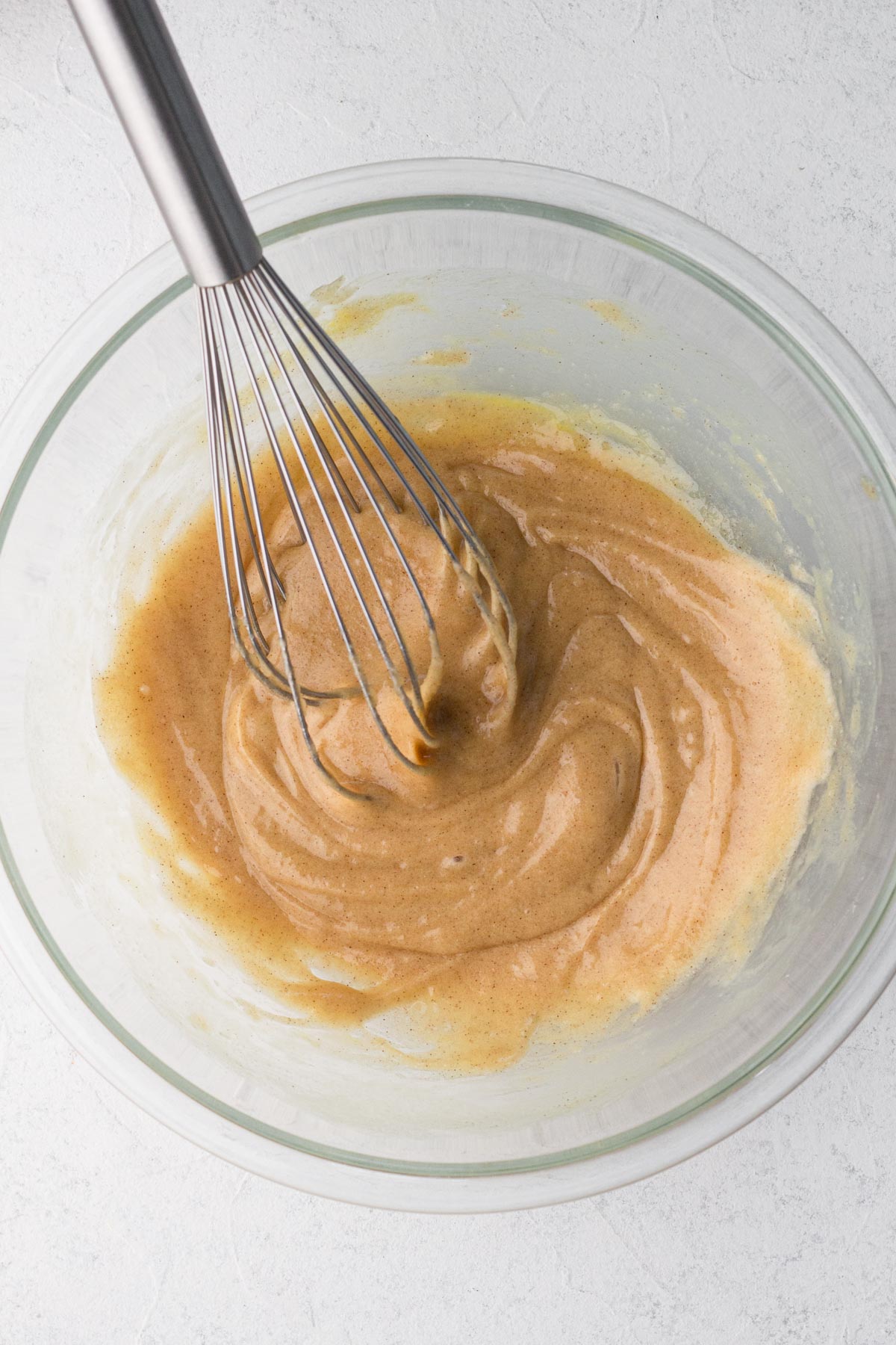 Cake batter in a glass mixing bowl with a metal whisk.