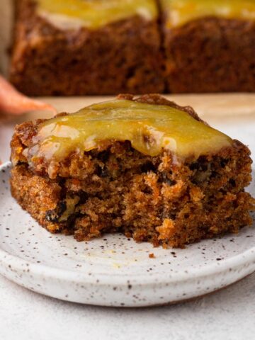 A square slice of carrot cake topped with orange glaze with a bite missing.