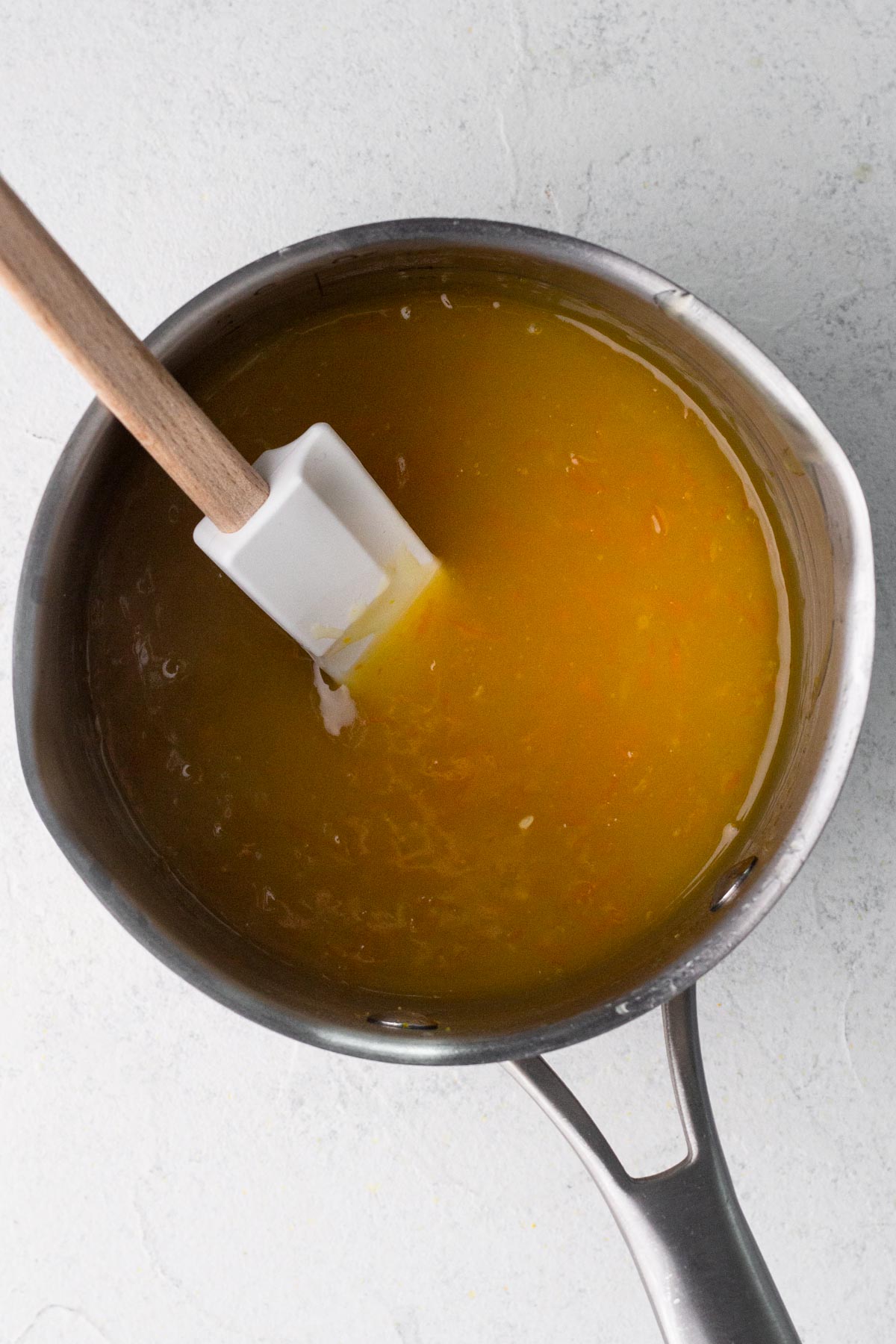 Orange glaze in a saucepan with a rubber spatula.
