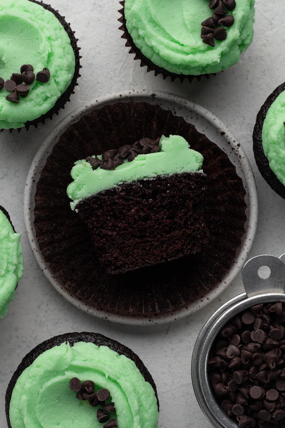 Half of a chocolate cupcake topped with green frosting and chocolate chips on a speckled plate.