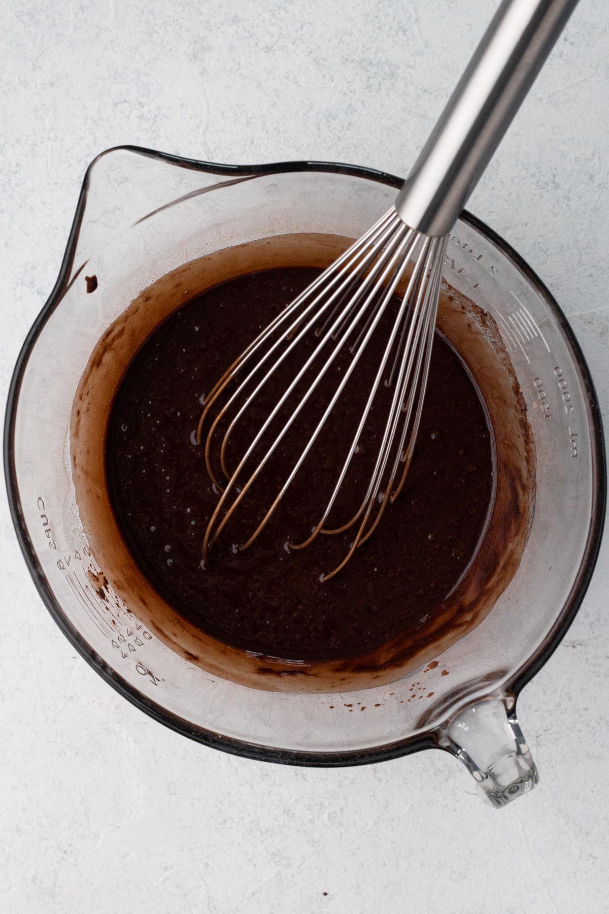Chocolate cupcake batter in a glass batter bowl with a metal whisk.