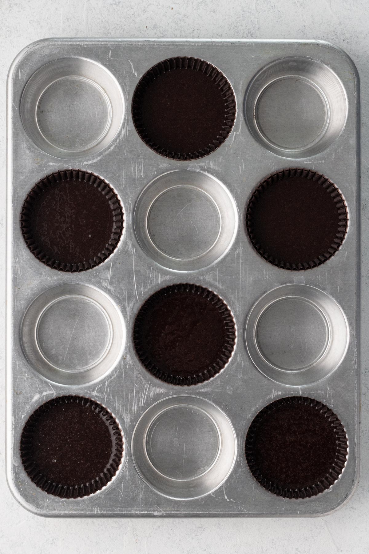 Cupcake batter in dark brown cupcake liners in a metal cupcake pan.
