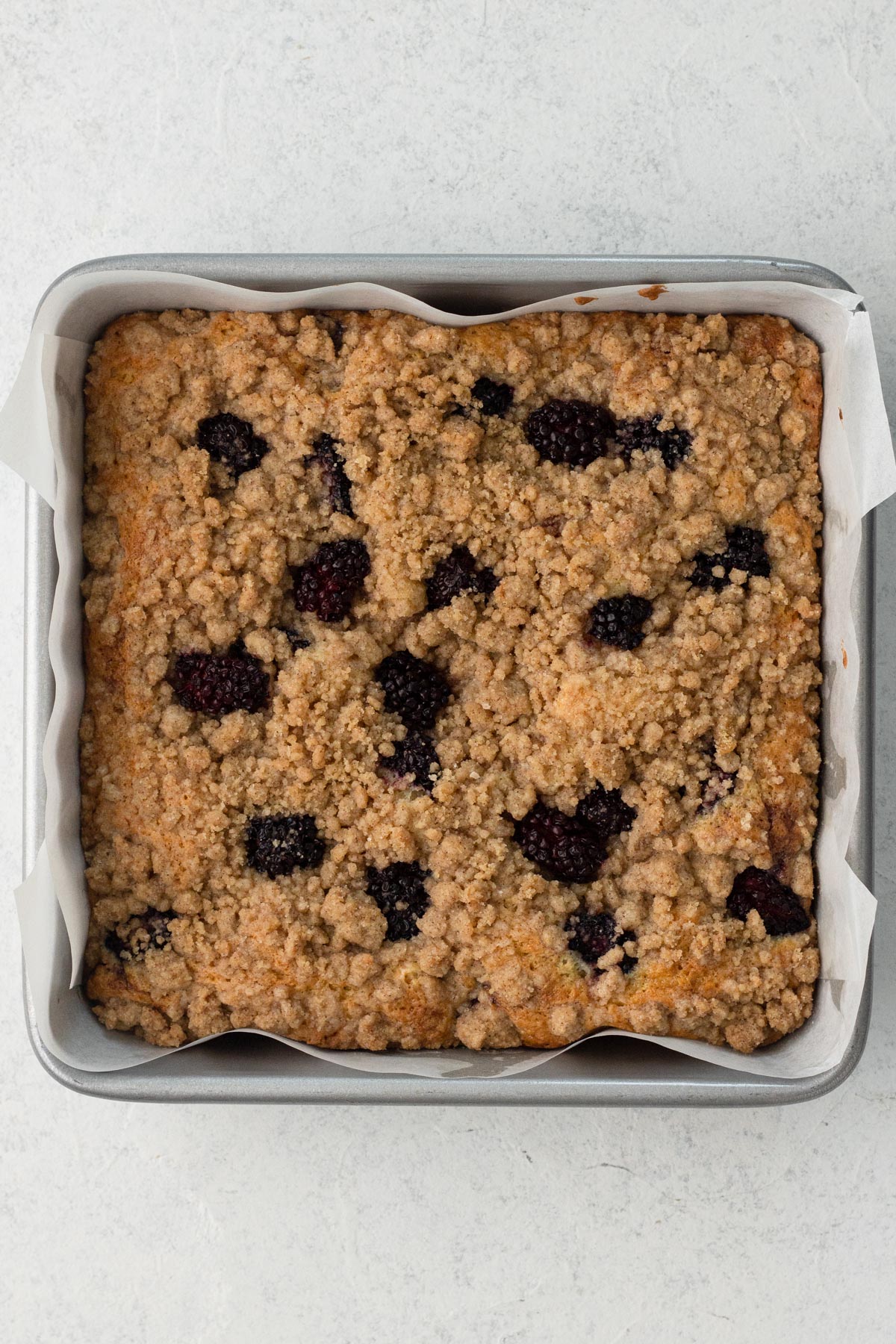 Baked coffee cake with blackberries in a square metal baking pan.