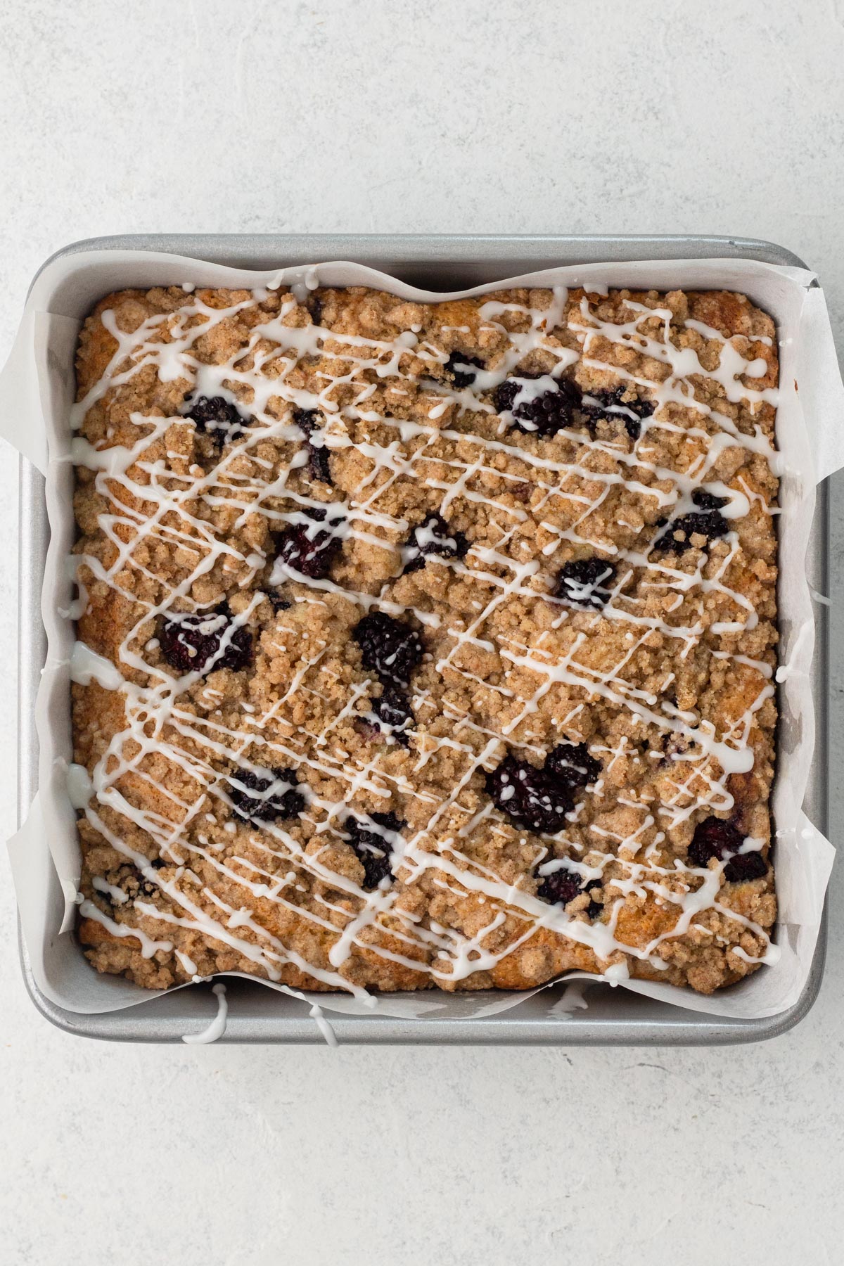 Glaze drizzled over coffee cake in a square metal baking pan.