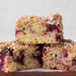 Slices of coffee cake swirled with blackberries stacked on a wooden cutting board.