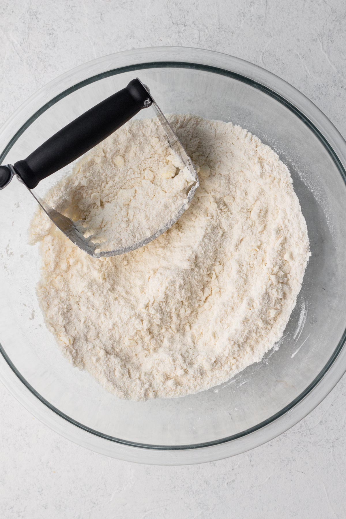 Butter cut into dry ingredients in a glass mixing bowl with a pastry cutter.