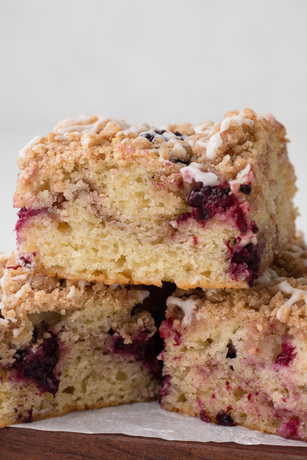 Square slices of coffee cake swirled with blackberries stacked on a wooden cutting board.