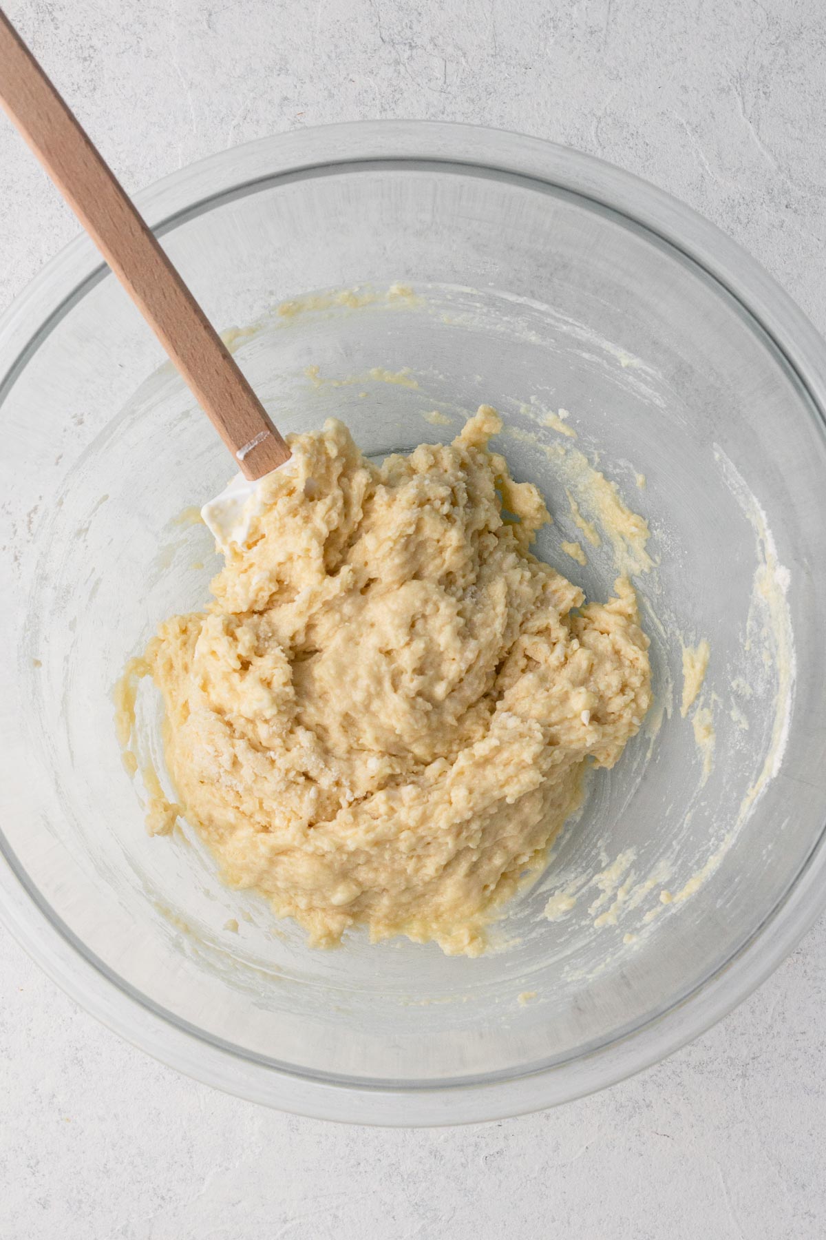Cake batter in a glass mixing bowl with a wooden spoon.