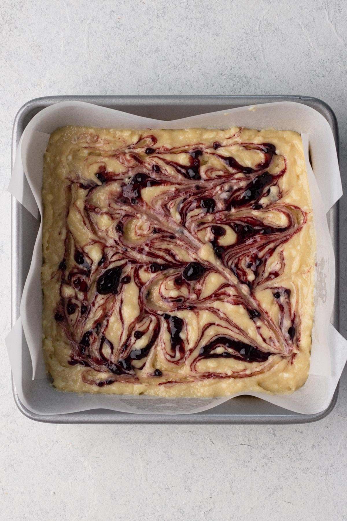 Preserves swirled into cake batter in a square metal baking pan.