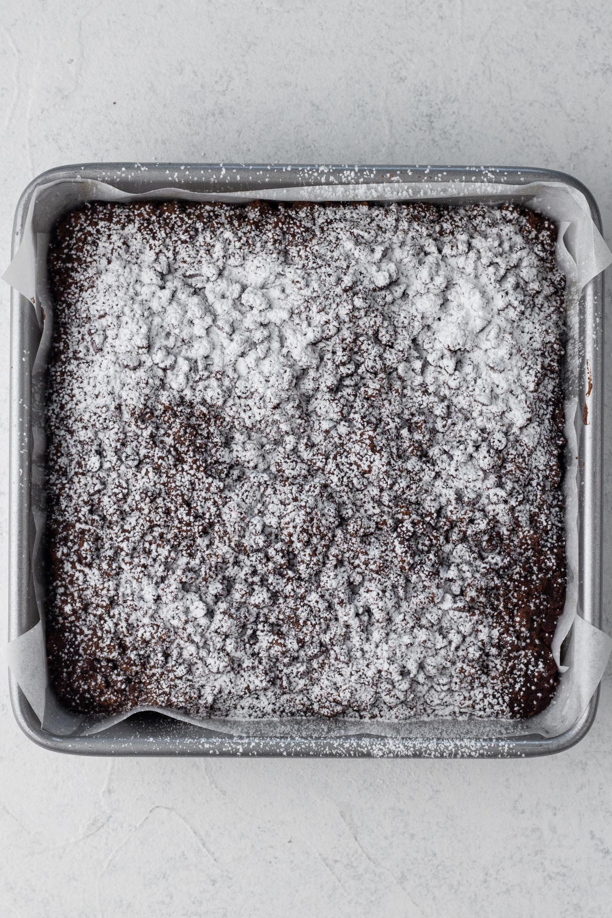 Cake dusted with confectioners' sugar in a square metal baking pan.