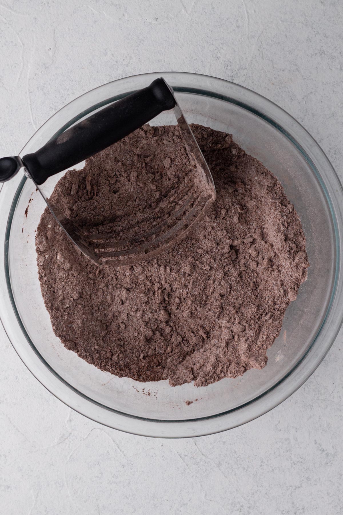 Butter cut into dry ingredients in a glass mixing bowl with a pastry cutter.