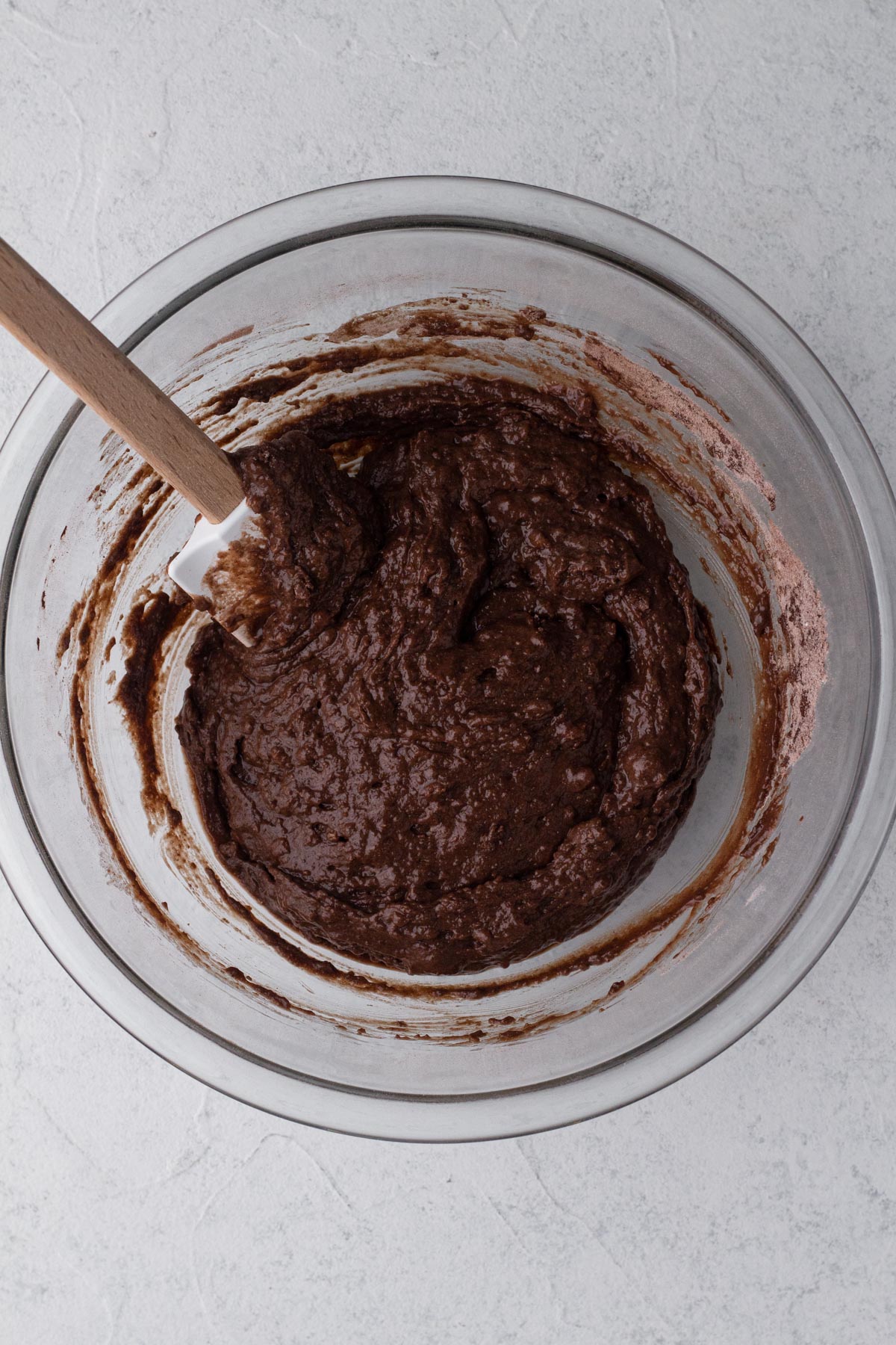Cake batter in a glass mixing bowl with a wooden spoon.