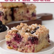 A square slice of coffee cake with blackberries and a drizzle of glaze on a white plate with a text overlay.