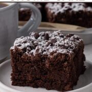 A slice of chocolate crumb cake on a white plate next to a cup of coffee with a text overlay.