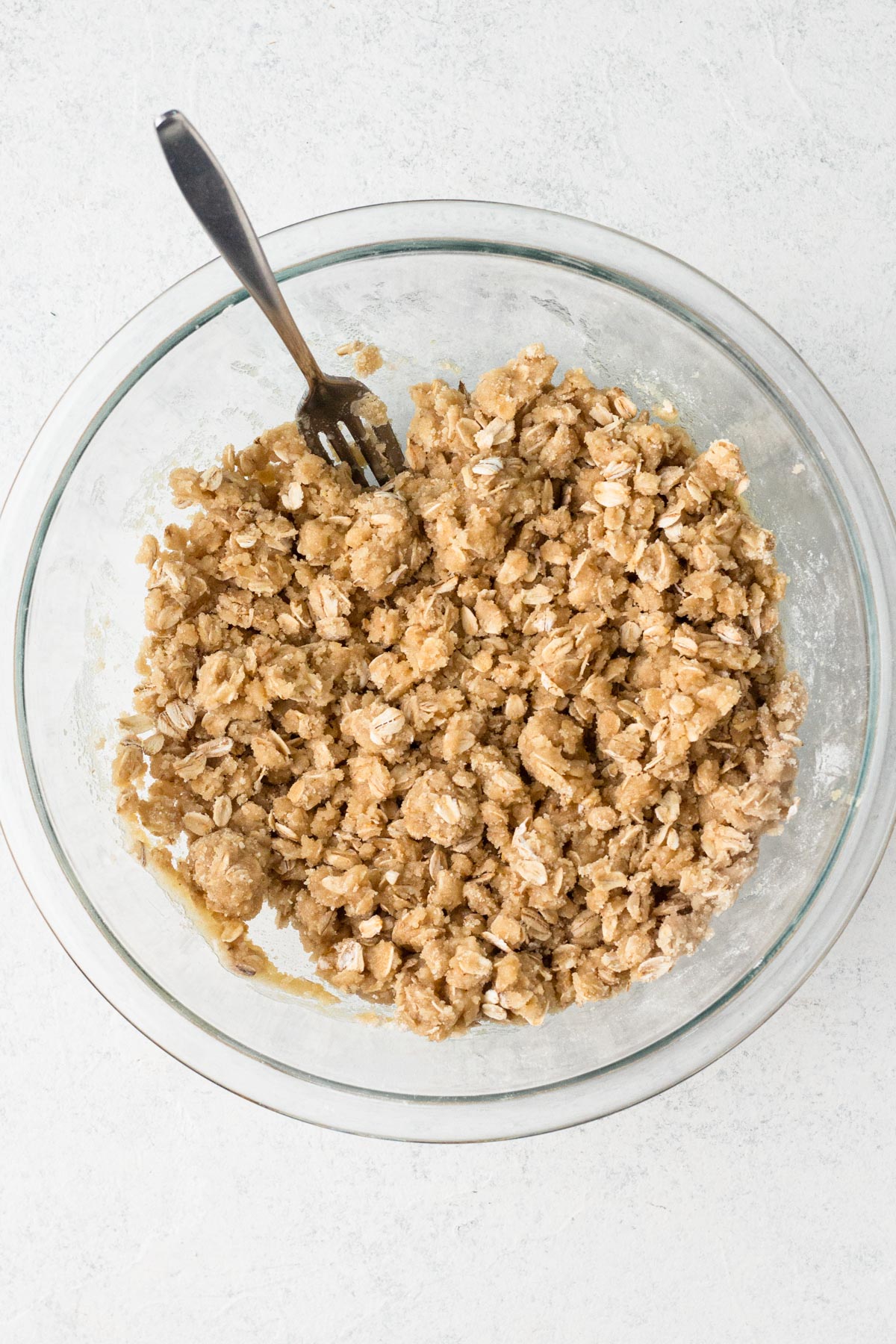 Crumble dough in a glass mixing bowl with a fork.