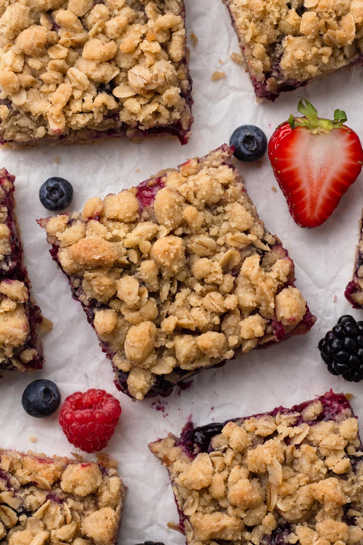 Bars filled with fruit and topped with crumble on crinkled parchment paper with pieces of fresh fruit.