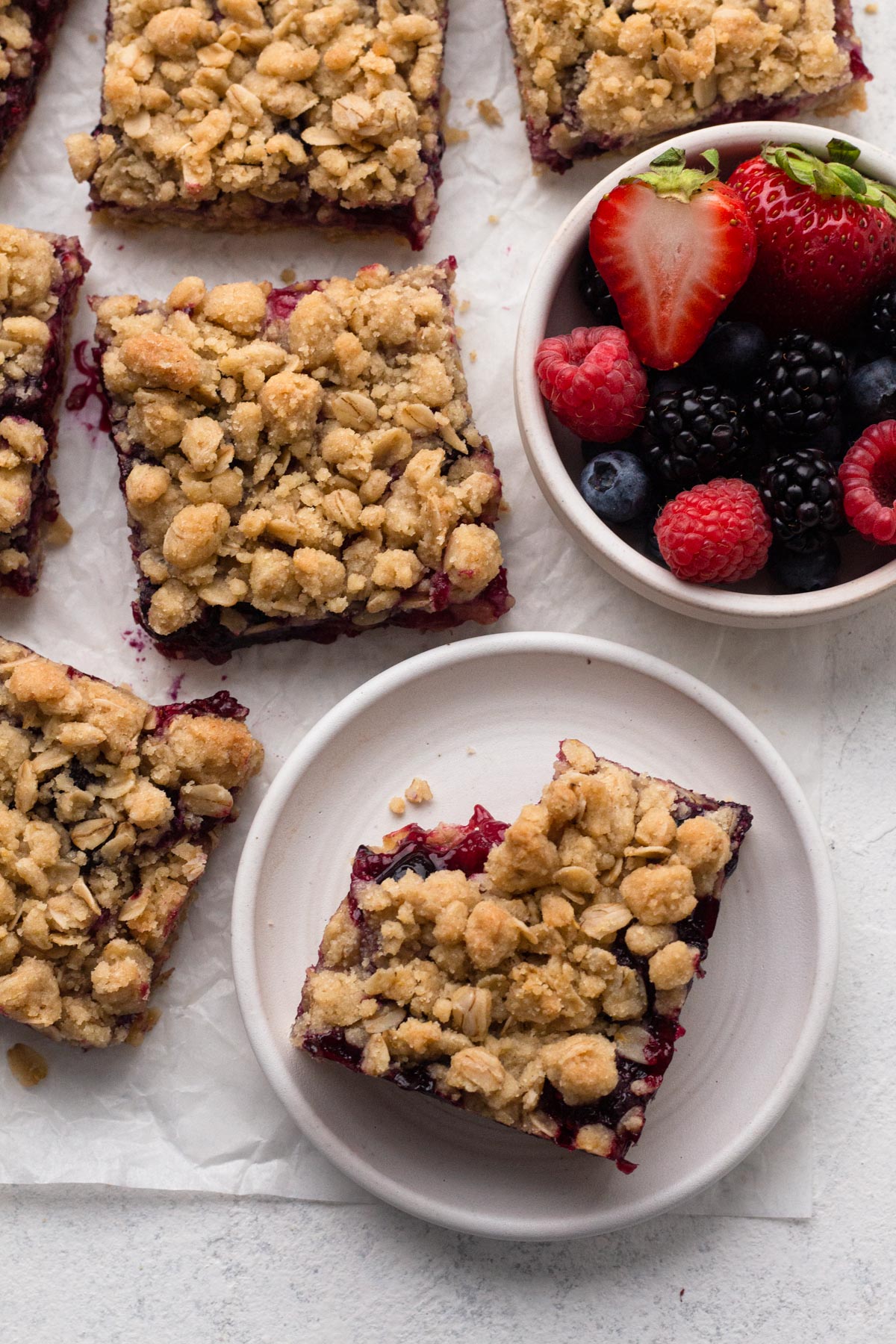 A bitten, fruit-filled bar topped with crumble with a bowl of fresh fruit.