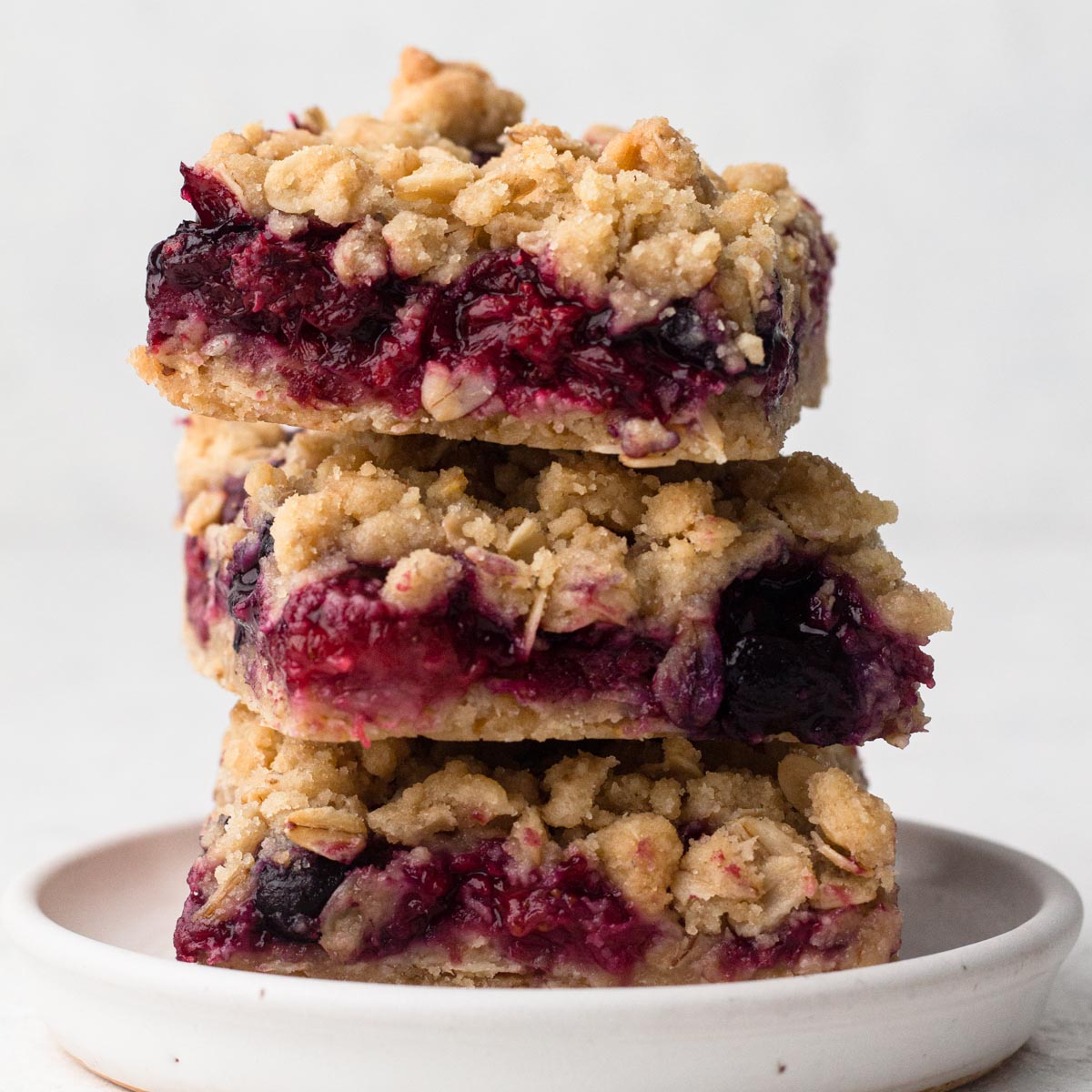 Berry-filled crumble bars stacked on a white plate.