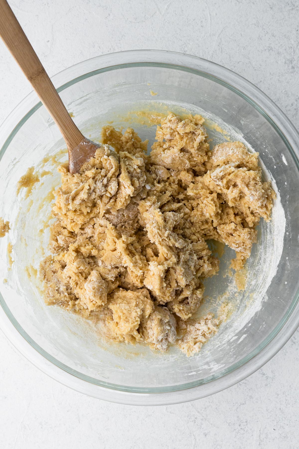 Cookie dough in a glass mixing bowl with a wooden spoon.