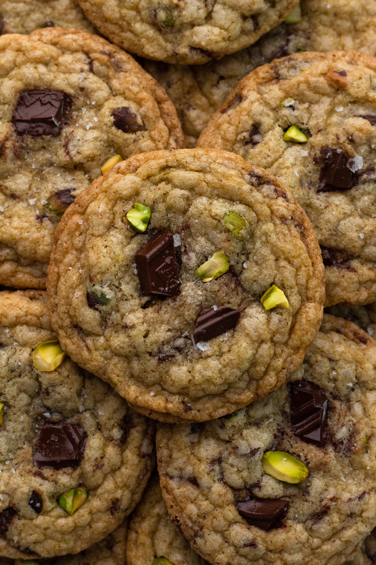 Cookies with bits of chocolate and chopped pistachios stacked on top of each other.