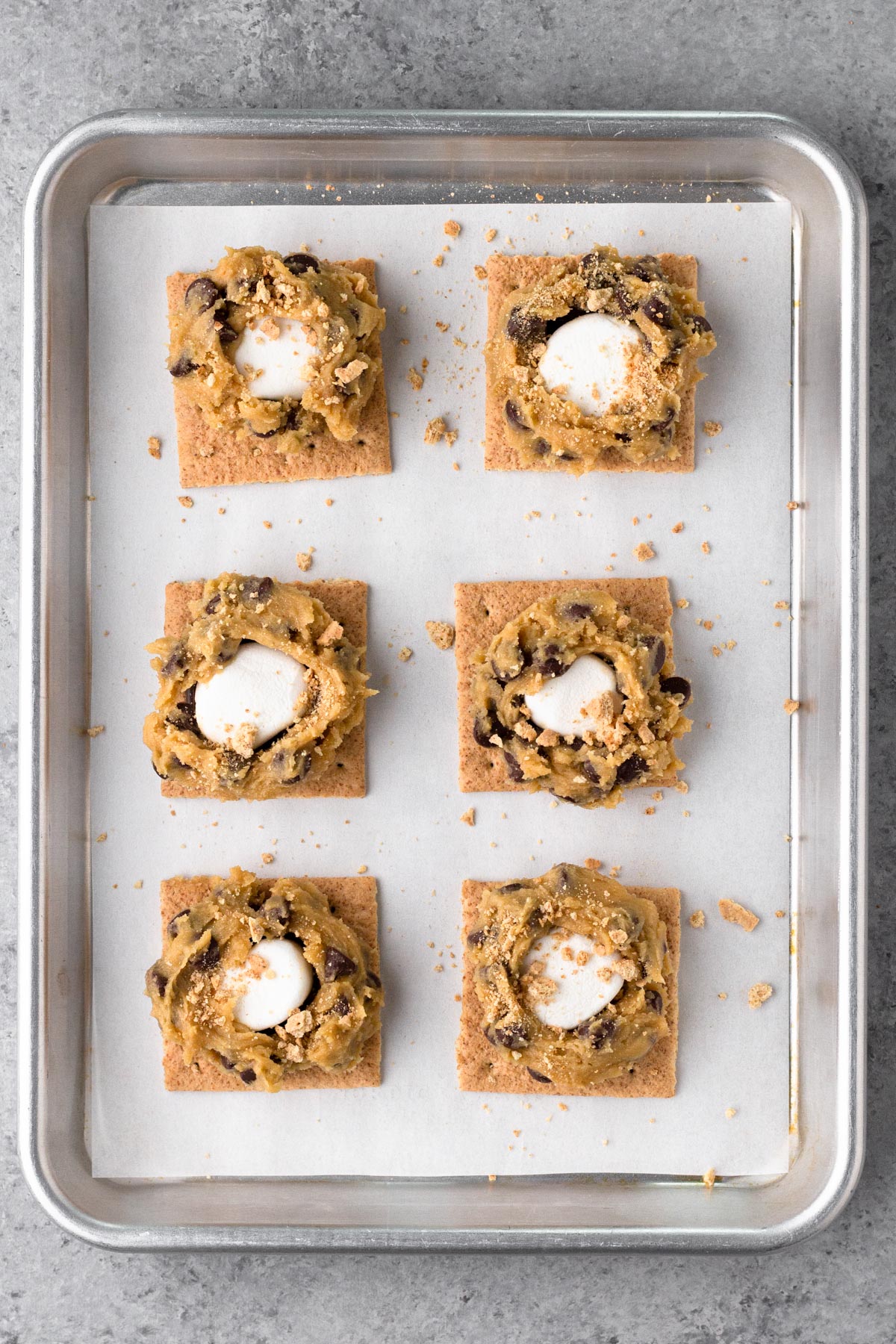 Assembled s'mores cookies with graham crackers and marshmallows on a baking sheet.